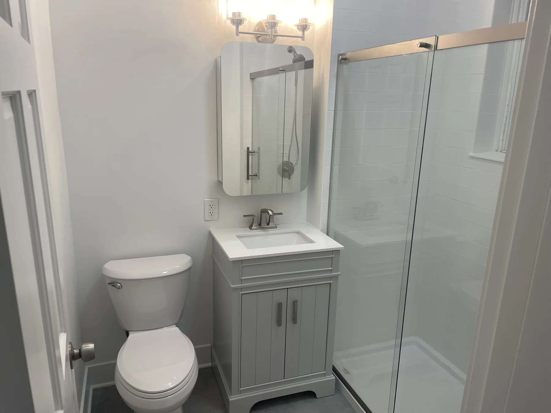 Compact remodeled bathroom with glass shower and gray vanity