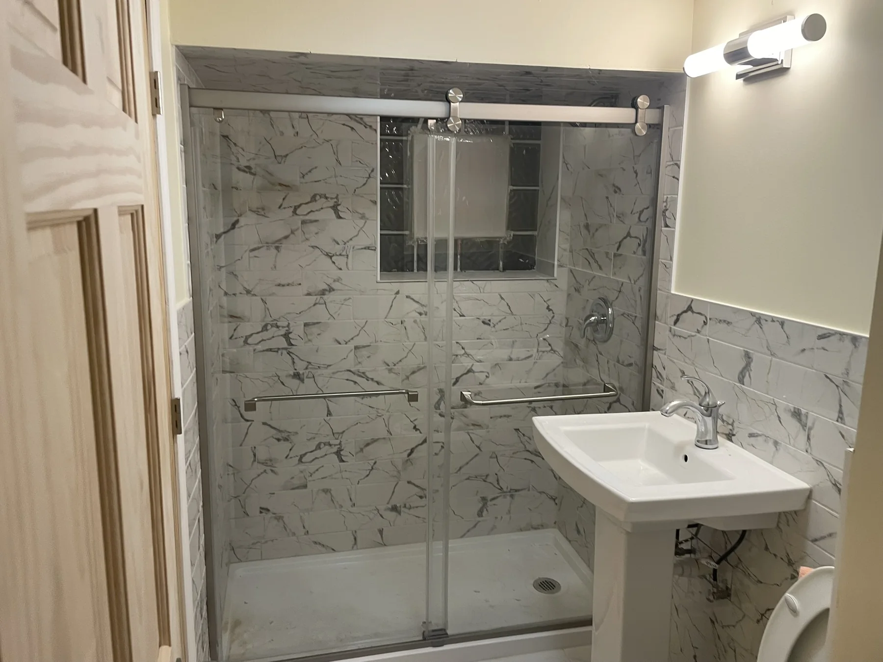 Bathroom with marble-look shower tile, sliding glass doors, and pedestal sink
